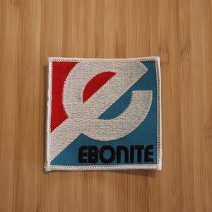 May include: A white, blue, and red embroidered patch with the word "Ebonite" in black lettering.