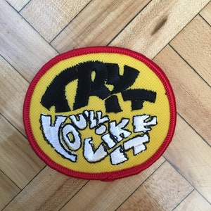 May include: A yellow and red circular patch with black and white embroidery. The text on the patch reads "TRY IT YOU'LL LIKE IT".