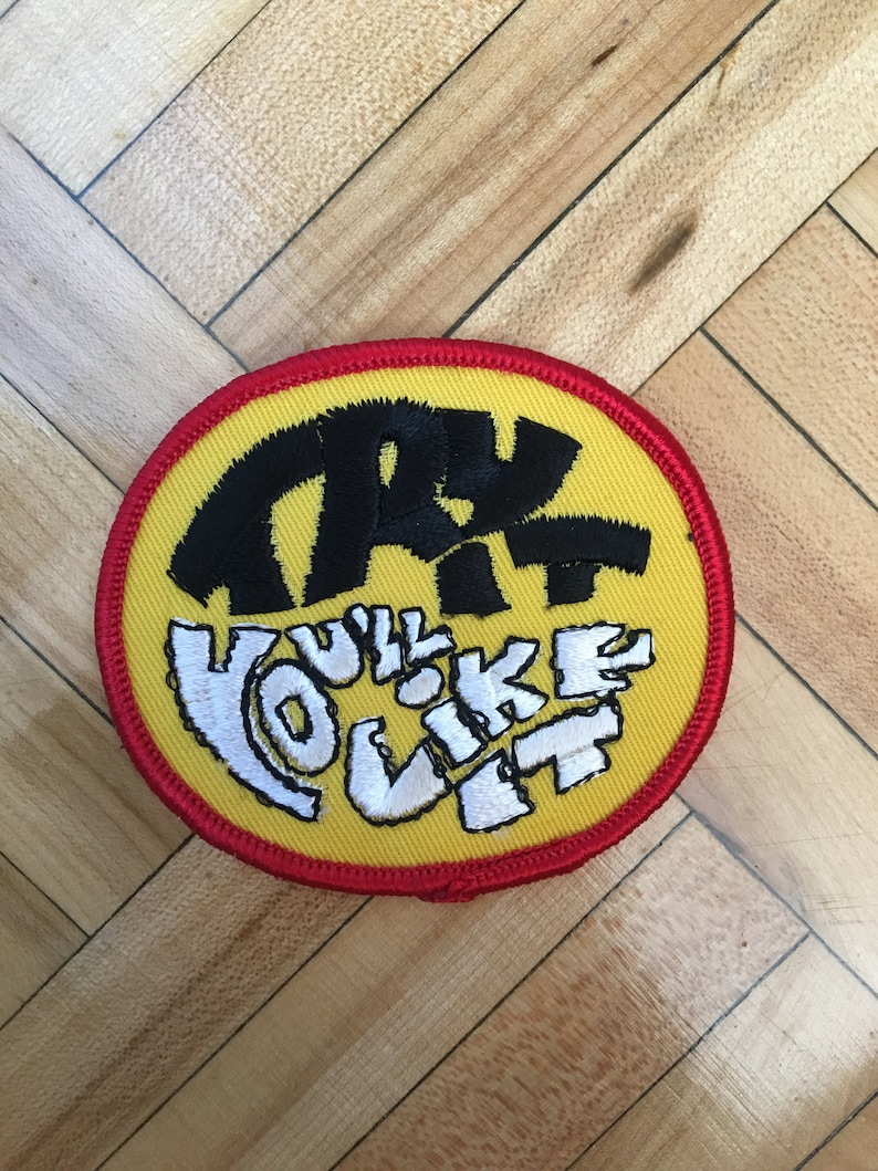 May include: A yellow and red circular patch with black and white embroidery. The text on the patch reads "TRY IT YOU'LL LIKE IT".