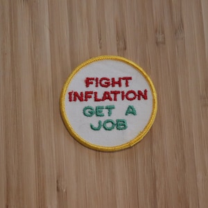 May include: A white round patch with a yellow border. The text "FIGHT INFLATION GET A JOB" is embroidered in red and green.