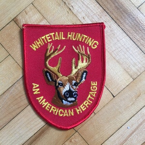 Può includere: Toppa ricamata rossa con un cervo dalla coda bianca e il testo "Whitetail Hunting An American Heritage" in giallo.