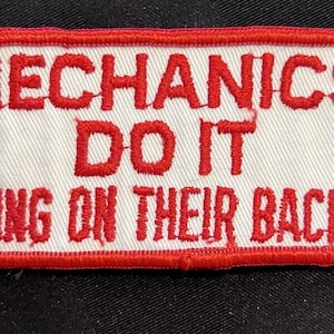 May include: Red embroidered patch with a white background. The text reads "Mechanics Do It Lying On Their Backs".