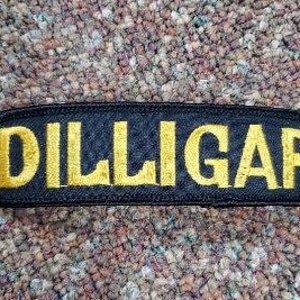 May include: Black patch with the word "DILLIGAF" embroidered in gold thread.