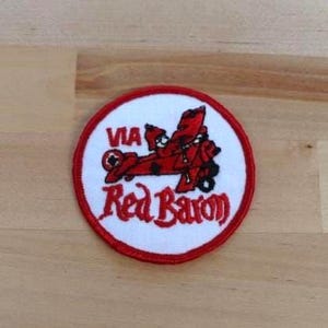 May include: A red, white, and blue embroidered patch with a red airplane and the text "VIA Red Baron".