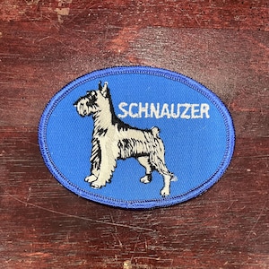 May include: Blue oval-shaped patch with white embroidered text "SCHNAUZER" and a black and white embroidered image of a Schnauzer dog.