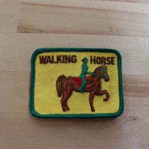 May include: A yellow embroidered patch with green trim featuring a brown horse with a rider and the text "WALKING HORSE".