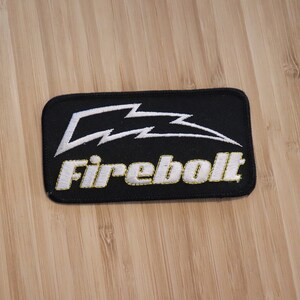 Può includere: Toppa ricamata nera con un fulmine bianco e la parola "Firebolt" in bianco con un contorno giallo.