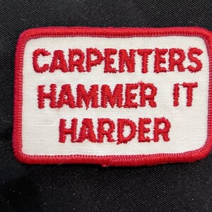 Peut inclure: Écusson brodé rouge et blanc avec le texte "CARPENTERS HAMMER IT HARDER".