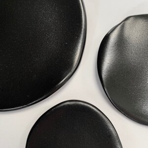 Puede incluir: Primer plano de tres platos de cer&aacute;mica negros de formas irregulares. Los platos tienen un acabado mate y est&aacute;n dispuestos sobre un fondo blanco. Los platos son probablemente para servir comida.
