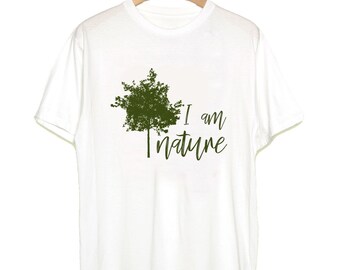May include: White t-shirt with a green tree graphic and the text "I am nature". The design features a stylized tree silhouette with a handwritten font. The shirt is hanging on a wooden hanger.