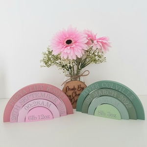 May include: Two wooden rainbow arches with engraved details. The pink arch is for Freya Lily Knott, born September 26, 2013, at 12:28 AM, weighing 6 pounds 12 ounces. The green arch is for Ryver Colville, born March 1st, 2022, at 12:55 AM, weighing 8 pounds 3 ounces.