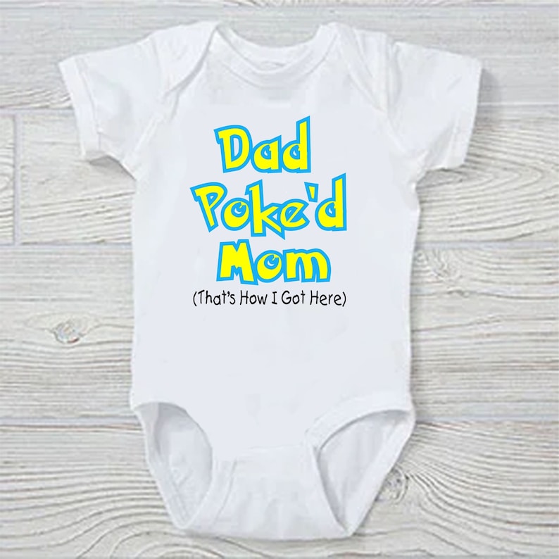Pu&ograve; includere: Body bianco per neonato con testo blu e giallo che dice "Dad Poke'd Mom (That's How I Got Here)"