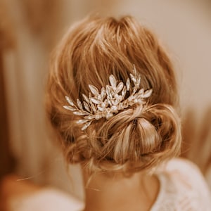 May include: A gold hair comb with clear crystal and pearl accents. The comb is in the shape of a leafy branch.