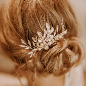 May include: A gold hair comb with a delicate floral design and pearl accents. The comb is adorned with clear crystals and is perfect for adding a touch of elegance to any hairstyle.