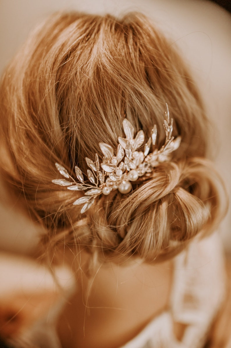 May include: A gold hair comb with a delicate floral design and pearl accents. The comb is adorned with clear crystals and is perfect for adding a touch of elegance to any hairstyle.