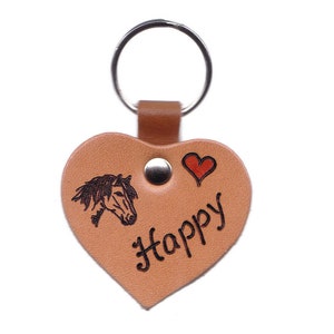 Könnte beinhalten: Ein brauner Leder-Schlüsselanhänger in Herzform mit einem Pferdekopf-Design, dem Wort "Happy" und einem kleinen roten Herz.