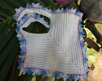 May include: A handmade white crochet bib with a scalloped edge in blue and pink. The bib has a square shape with a neck strap, suitable for a baby or toddler. The crochet work is detailed and the colours are soft.