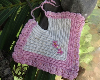 May include: Handmade crochet baby bib in white and pink. The bib features a scalloped pink border and a small floral embroidery. The bib is made of soft yarn and has a tie closure at the neck.