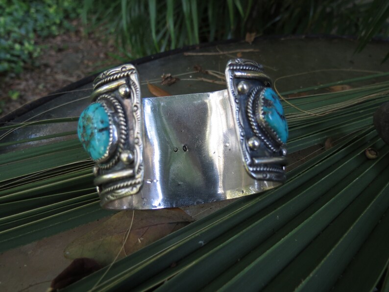 May include: A silver cuff bracelet with two turquoise stones set in silver. The bracelet is decorated with intricate silver designs.