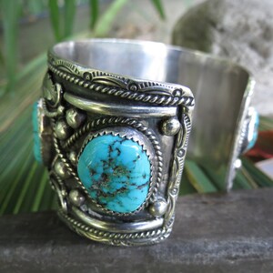 May include: A silver cuff bracelet with turquoise stones set in the metal. The bracelet has intricate designs and is a beautiful piece of jewelry.