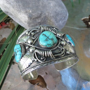 May include: A silver cuff bracelet with intricate designs and three turquoise stones.