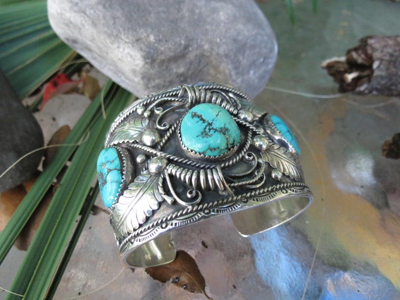 May include: A silver cuff bracelet with intricate designs and three turquoise stones.