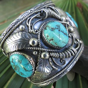 May include: A silver cuff bracelet with three turquoise stones set in the center. The bracelet is decorated with intricate silverwork, including leaves and swirls.