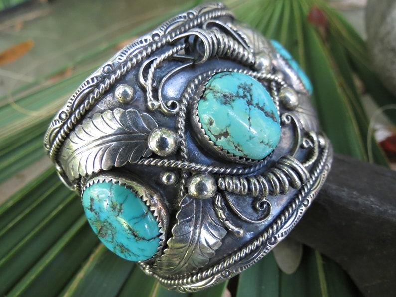 May include: A silver cuff bracelet with three turquoise stones set in the center. The bracelet is decorated with intricate silverwork, including leaves and swirls.