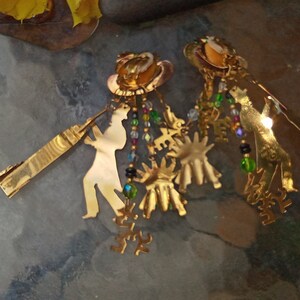 May include: Gold tone earrings with a silhouette of a person playing a musical instrument, with dangling charms and beads.