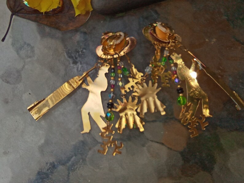 May include: Gold tone earrings with a silhouette of a person playing a musical instrument, with dangling charms and beads.