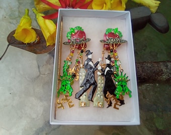 May include: A pair of dangle earrings with a red apple charm with the words "New York" on it. The earrings also feature a black and white silhouette of a couple dancing, a green Statue of Liberty charm, and gold accents.