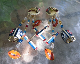 May include: Unique dangle earrings featuring football-themed charms. The earrings showcase miniature football helmets, footballs, and goalposts, accented with colorful beads. The design incorporates gold-tone metal and patriotic colors.