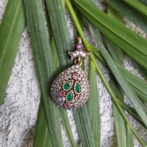 May include: A silver pendant with a teardrop shape, adorned with clear and pink cubic zirconia stones. The pendant features a green stone design in the center and a small star charm at the top.