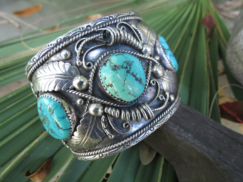 May include: A silver cuff bracelet with intricate designs and turquoise stones. The bracelet is decorated with a rope-like border and floral patterns.