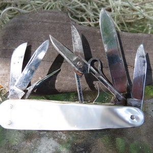 May include: A multi-tool knife with a pearlescent white handle and multiple stainless steel blades and tools. The tools include a variety of blades, scissors, and other implements. The knife is open, displaying all of its tools.