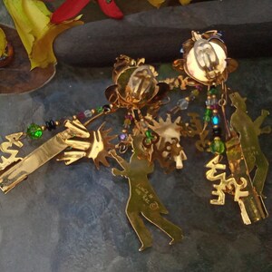 May include: A pair of gold-tone dangle earrings with a variety of charms, including a silhouette of a person, a palm tree, and a star. The earrings are adorned with colorful beads and crystals.