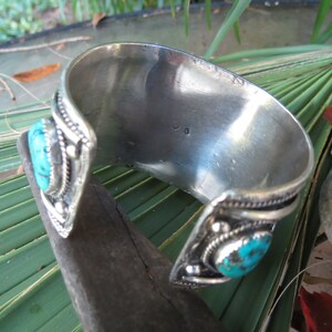 May include: Silver cuff bracelet with turquoise stones and intricate detailing. The bracelet is open and has a silver stamp on the inside.