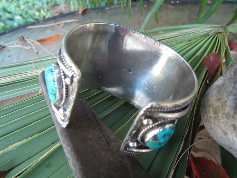 May include: Silver cuff bracelet with turquoise stones and intricate detailing. The bracelet is open and has a silver stamp on the inside.