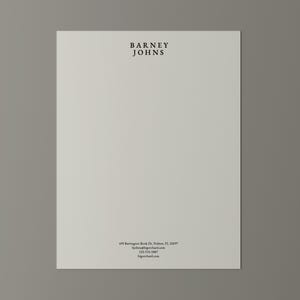 May include: A cream-coloured sheet of paper with the text "BARNEY JOHNS" in black at the top. Additional black text at the bottom includes an address, phone number, and website.