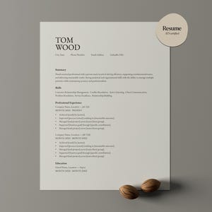 Może przedstawiać: Kremowe CV zatytułowane "Resume 175 Certified" z imieniem "TOM WOOD" na górze. CV zawiera sekcje podsumowania, umiejętności, doświadczenia i wykształcenia. Dwa orzechy włoskie znajdują się na dole.