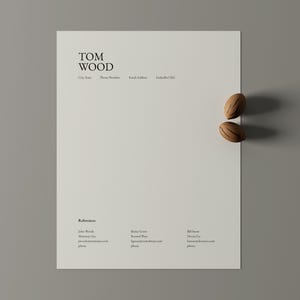 以下が含まれることがあります： 「TOM WOOD」という名前が上部に記載されたミニマリストの履歴書テンプレート。連絡先情報も含まれています。2つの装飾的な木製のオブジェクトが紙の右側に配置されています。履歴書には、参照用のセクションが含まれています。