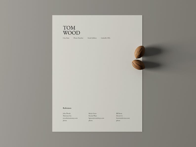 May include: A minimalist CV template featuring the name "TOM WOOD" at the top, with contact details. Two decorative wooden objects are positioned on the right side of the paper. The CV includes a section for references.