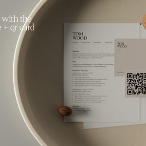 Op de afbeelding: Een cv en visitekaartje met de naam "TOM WOOD" erop gedrukt, samen met een QR-code en een kleine, ronde sticker met de tekst "Level up". Het cv staat op wit papier en de visitekaart is lichtbeige.