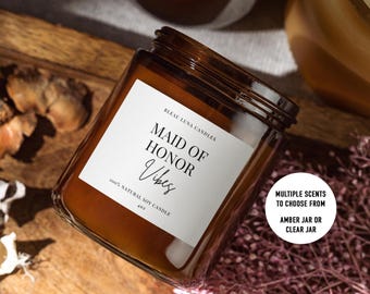 Op de afbeelding: Een bruine glazen kaars pot met een wit label waarop staat "BLEAU LUNA CANDLES MAID OF HONOR Vibes 100% NATURAL SOY CANDLE 40z". De kaars pot staat op een houten oppervlak. Een witte cirkel met zwarte tekst luidt "MULTIPLE SCENTS TO CHOOSE FROM AMBER JAR OR CLEAR JAR".