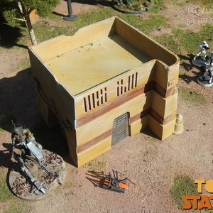 May include: A beige, two-story building with a flat roof and a brown door. The building has a brown trim and several windows. The building is surrounded by green grass and a few small trees. The text "BLACK SPIRE OUTPOST" is visible in the upper right corner of the image. The text "TOSSCHE STATION" is visible in the lower right corner of the image.