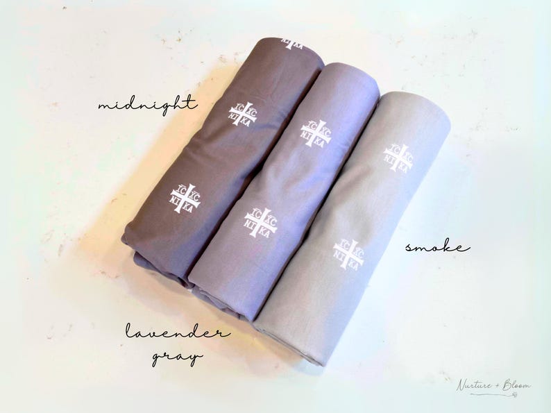 Pu&ograve; includere: Tre campioni di tessuto in tonalit&agrave; di grigio, etichettati "midnight", "lavender gray" e "smoke". Ogni campione presenta una croce bianca ricamata.