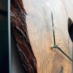 May include: A wooden clock with a black frame and black hands. The clock face is a natural wood slice with a unique grain pattern.