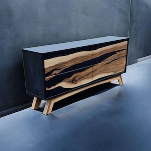 May include: A black dresser with four drawers made of wood and resin. The drawers have a natural wood grain pattern with black resin accents. The dresser has four wooden legs.