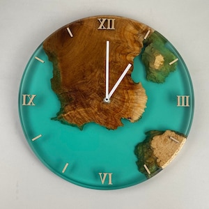 Può includere: Orologio da parete rotondo con sfondo in resina turchese e centro in legno venato. L'orologio presenta numeri romani e lancette in legno. La venatura del legno è marrone naturale e le lancette sono bianche.