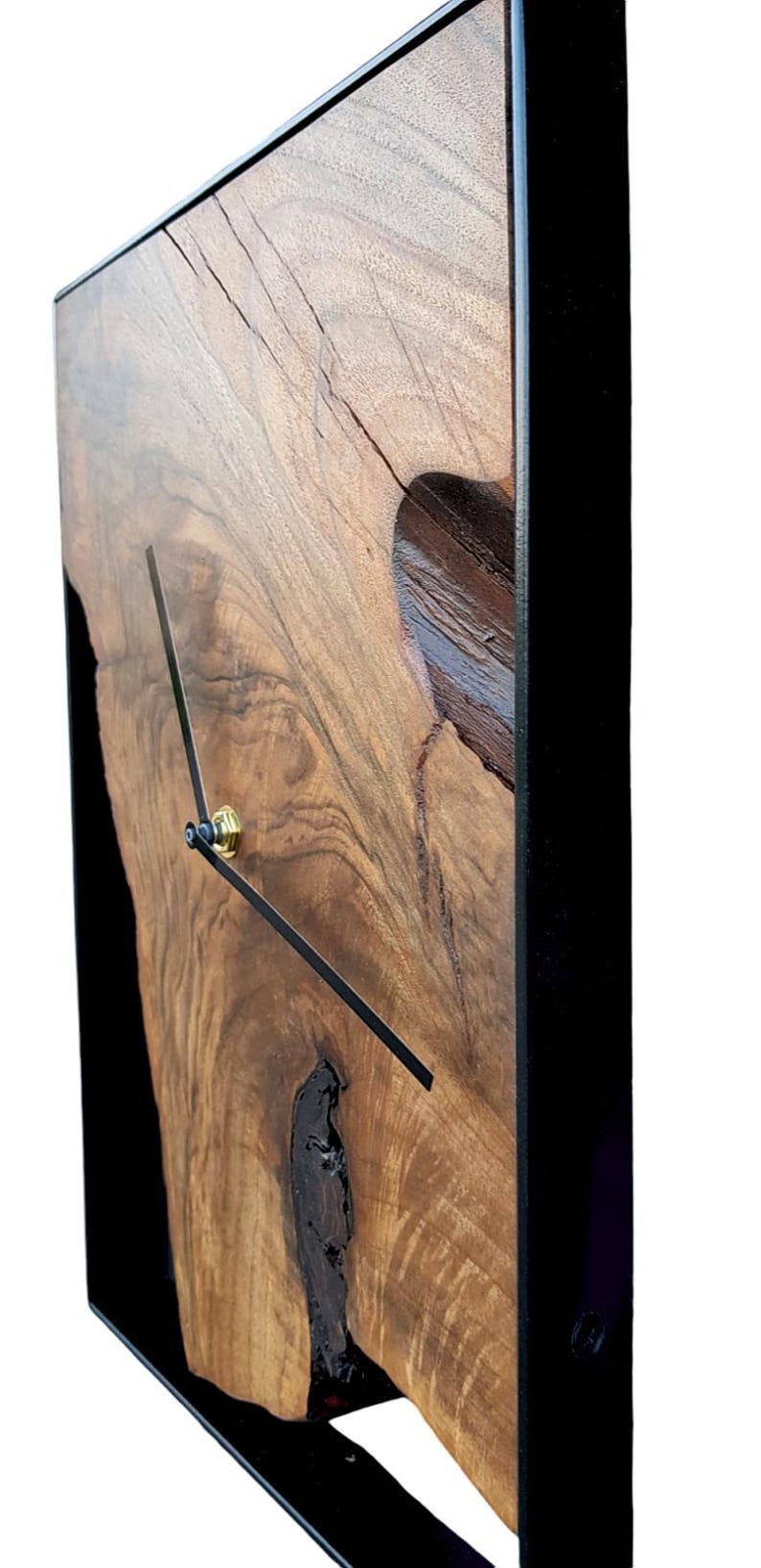 May include: A wooden wall clock with a black metal frame. The clock face is made of a natural wood slice with a unique grain pattern. The clock hands are black and the clock has a gold knob.